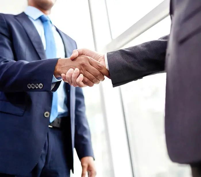 Two men in suits shaking hands over a window.