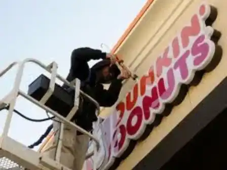 A man on a crane painting the dunkin donuts sign.